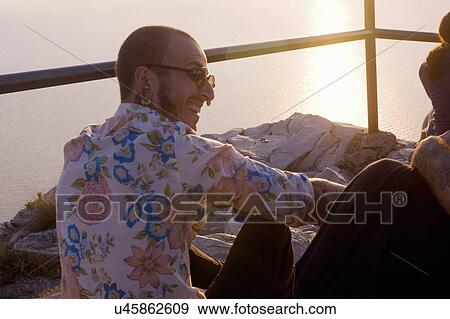 Stock Photo - Two young men sitting chatting at coast, Marseille, France. Fotosearch