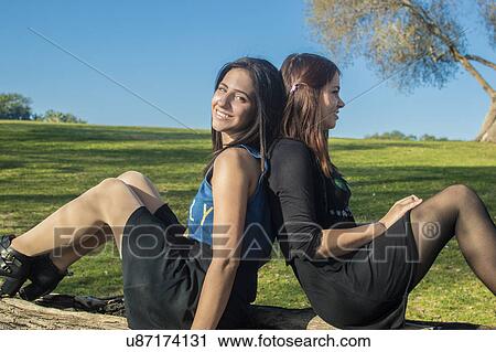 Stock Image - Two young women in field, sitting back to back. Fotosearch