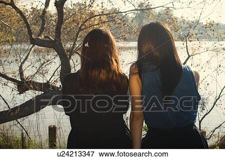Two young women sitting beside lake, rear view View Large Photo Image Stock Photo - Two young women sitting beside lake, rear view. Fotosearch