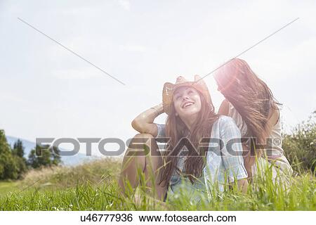 Stock Photograph - Two young women sitting chatting in grassy field. Fotosearch