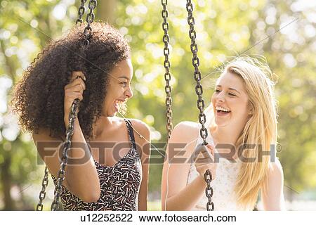Two young women sitting on park swing laughing View Large Photo Image Stock Image - Two young women sitting on park swing laughing. Fotosearch