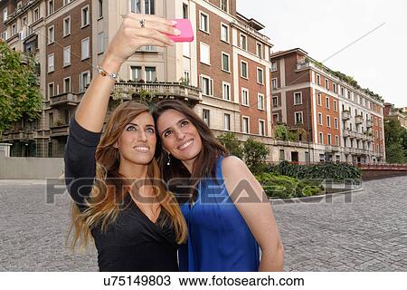 Two young women taking self portrait using smartphone View Large Photo Image Stock Image - Two young women taking self portrait using smartphone. Fotosearch