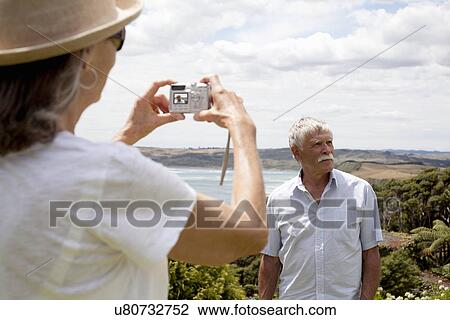 Stock Image - Wife photographing husband, ocean in background, Raglan, New Zealand. Fotosearch