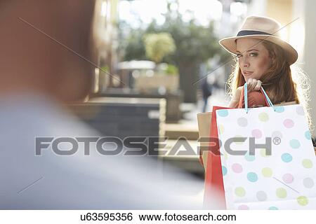 Woman holding shopping bags, looking over shoulder at man View Large Photo Image Stock Photograph - Woman holding shopping bags, looking over shoulder at man. Fotosearch