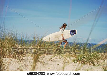 Stock Image - Woman with surfboard on beach, Lacanau, France. Fotosearch