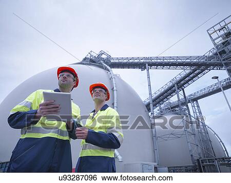 Workers using digital tablet at biomass facility, low angle view View Large Photo Image Stock Photograph - Workers using digital tablet at biomass facility, low angle view. Fotosearch