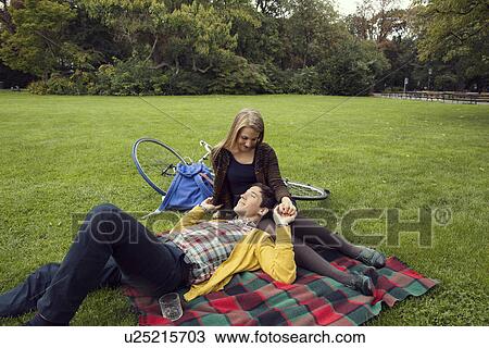 Stock Image - Young couple holding hands on picnic blanket in park. Fotosearch