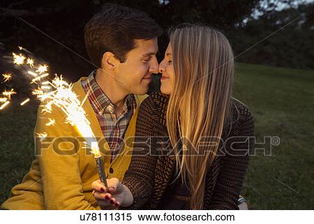 Young couple nose to nose in park holding sparkling firework View Large Photo Image Stock Photography - Young couple nose to nose in park holding sparkling firework. Fotosearch