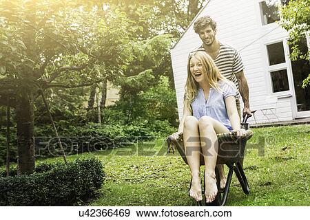 Stock Photo - Young couple playing with wheel barrow in garden. Fotosearch