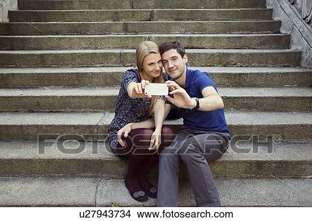 Young couple sitting on old street stairway posing for smartphone selfie View Large Photo Image Picture - Young couple sitting on old street stairway posing for smartphone selfie. Fotosearch
