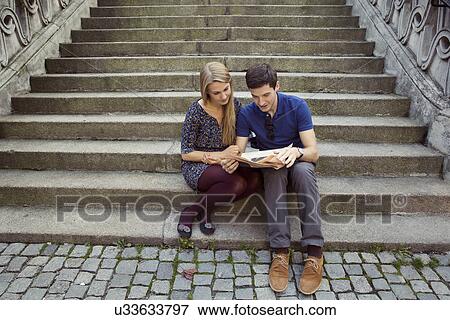 Stock Photo - Young couple sitting on old street stairway reading newspaper. Fotosearch