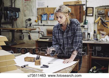 Stock Image - Young craftswoman checking components on workbench in pipe organ workshop. Fotosearch