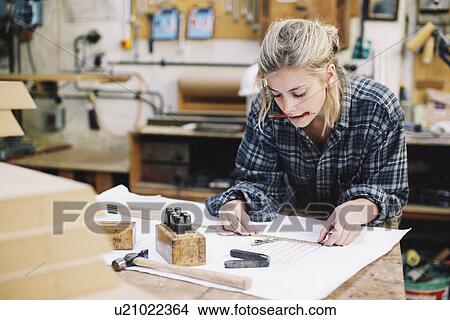 Picture - Young craftswoman measuring blueprint on workbench in pipe organ workshop. Fotosearch