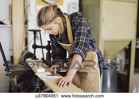 Stock Image - Young craftswoman using calculator in pipe organ workshop. Fotosearch