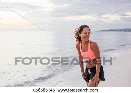 Stock Photography - Young female runner looking over shoulder and laughing on beach, Tuscany, Italy. Fotosearch