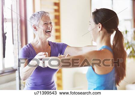 Stock Image - Young female student laughing with teacher in pilates gym. Fotosearch
