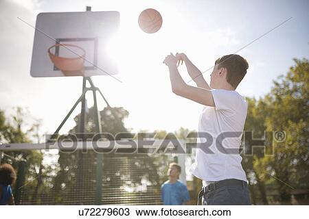 Stock Image - Young male basketball player throwing basketball into hoop. Fotosearch
