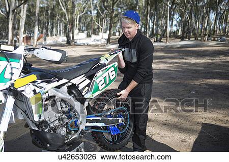 Young male motocross competitor lifting motorcycle in forest View Large Photo Image Stock Photograph - Young male motocross competitor lifting motorcycle in forest. Fotosearch