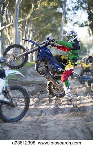 Stock Photograph - Young male motocross racer holding up motorcycle on forest track. Fotosearch