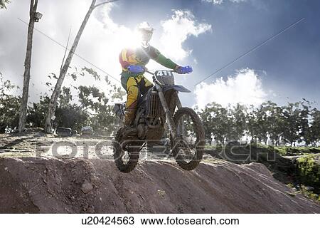 Stock Image - Young male motocross racer jumping mid air down mud hill. Fotosearch