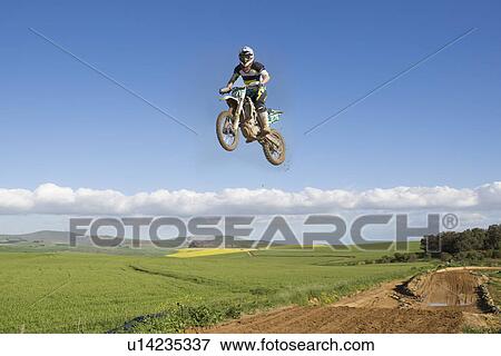 Stock Photo - Young male motocross racer jumping mid air over landscape. Fotosearch