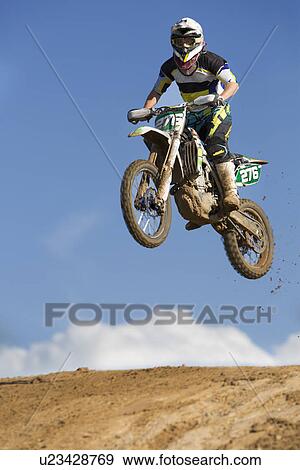 Stock Photo - Young male motocross racer jumping muddy hill. Fotosearch
