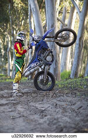 Young male motocross racer standing with motorcycle on forest track View Large Photo Image Stock Image - Young male motocross racer standing with motorcycle on forest track. Fotosearch