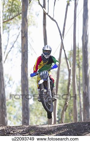 Stock Photo - Young male motocross rider jumping mid air in forest. Fotosearch