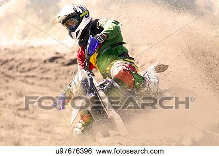 Stock Photograph - Young male motocross rider racing and leaning into mud track. Fotosearch