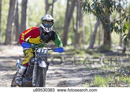 Stock Image - Young male motocross rider racing in forest. Fotosearch