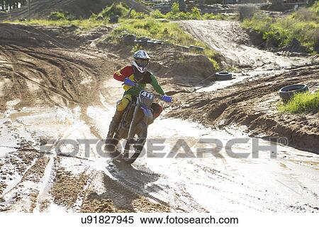 Young male motocross rider racing on muddy track View Large Photo Image Stock Photography - Young male motocross rider racing on muddy track. Fotosearch
