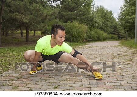 Picture - Young male runner crouching and stretching in park. Fotosearch