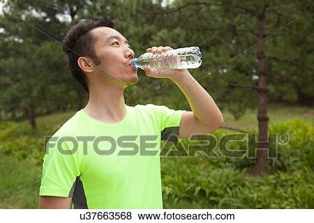 Stock Photo - Young male runner drinking bottled water in park. Fotosearch