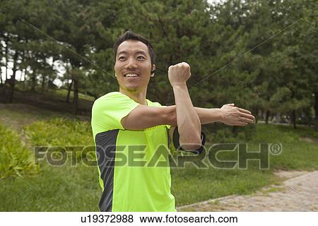 Stock Photo - Young male runner stretching arms in park. Fotosearch