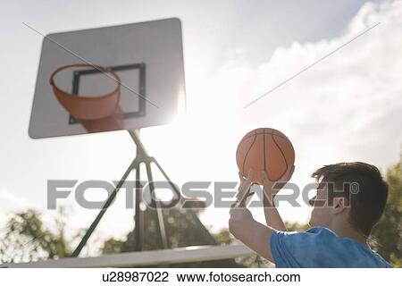 Stock Image - Young man aiming to throw basketball into basketball hoop. Fotosearch