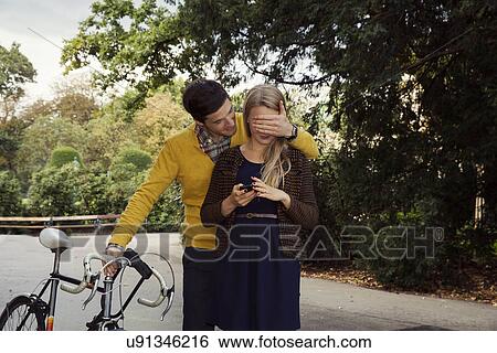 Stock Photograph - Young man covering girlfriends eyes in park. Fotosearch