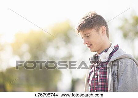 Picture - Young man in park with headphones around his neck. Fotosearch