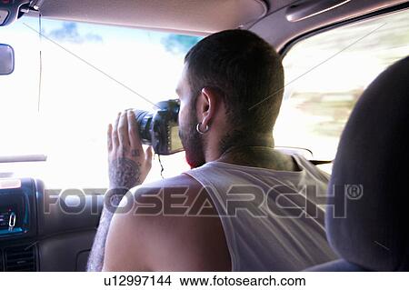 Picture - Young man taking photographs through car windscreen. Fotosearch
