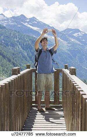 Stock Photography - Young man taking smartphone selfie in front of mountains, Formazza, Verbania, Piemonte, Italy. Fotosearch