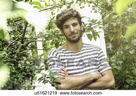 Stock Photo - Young man with arms crossed in garden. Fotosearch