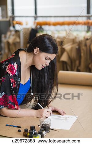Stock Photo - Young seamstress painting fashion design in workshop. Fotosearch