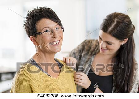 Stock Photograph - Young seamstress pinning shoulder of customers sweater in workshop. Fotosearch