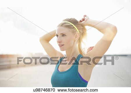 Stock Image - Young woman adjusting ponytail. Fotosearch