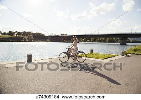 Picture - Young woman cycling at riverside, Danube Island, Vienna, Austria. Fotosearch