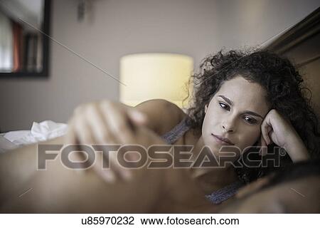 Stock Image - Young woman in bed with hand on man's shoulder. Fotosearch
