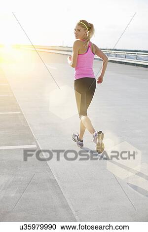 Young woman jogging, looking over shoulder View Large Photo Image Stock Image - Young woman jogging, looking over shoulder. Fotosearch