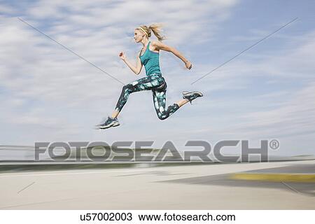 Stock Image - Young woman jumping mid air. Fotosearch