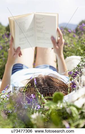Stock Photograph - Young woman lying in field reading book. Fotosearch