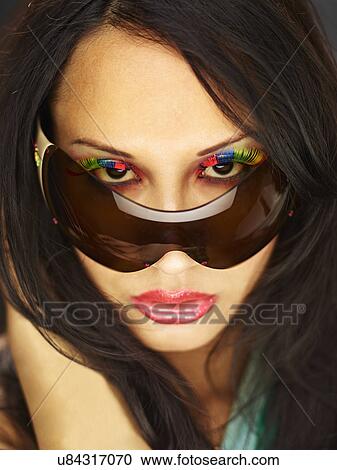 Stock Image - Young woman peeking over sunglasses with fake eyelashes. Fotosearch