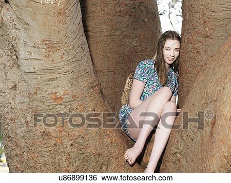 Stock Photograph - Young woman sitting in tree. Fotosearch